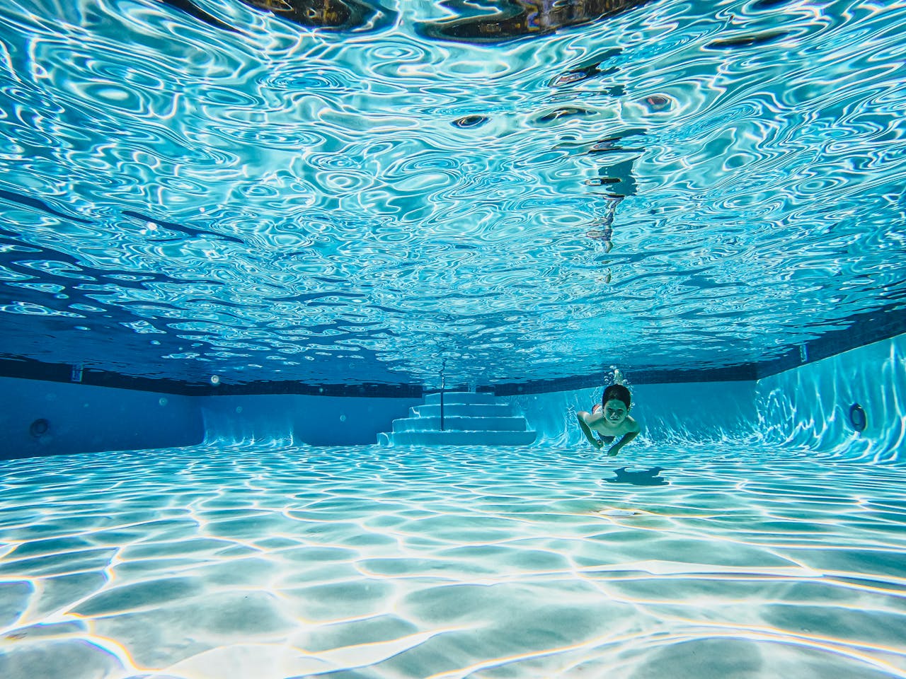 A young child swimming underwater in a clear blue pool, showcasing playful aquatic motions.